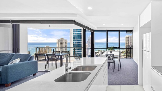 A modern kitchen with a large island, a dining area with a view of the city, and a living area with a sofa and a view of the ocean. - Circle on Cavill Ocean & River Views (Surfers Paradise)