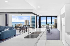 A modern kitchen with a large island, a dining area with a view, and a living area with a sofa. - Circle on Cavill Ocean & River Views (Surfers Paradise)