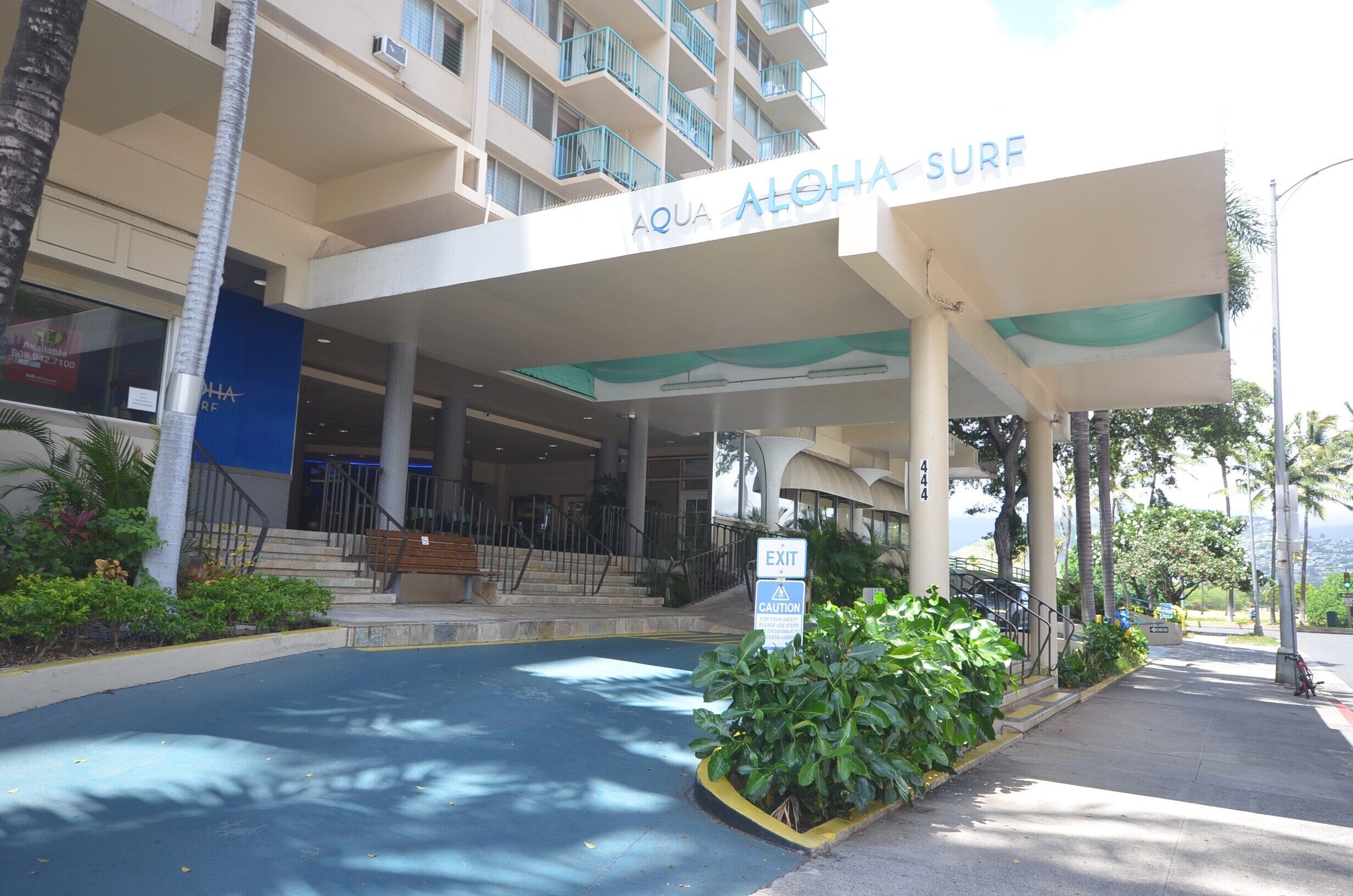 The entrance to Aqua Aloha Surf hotel with a covered walkway, palm trees, and a clear sky.