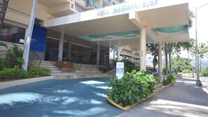De ingang van hotel Aqua Aloha Surf met een overdekte doorgang, palmbomen en een heldere lucht.