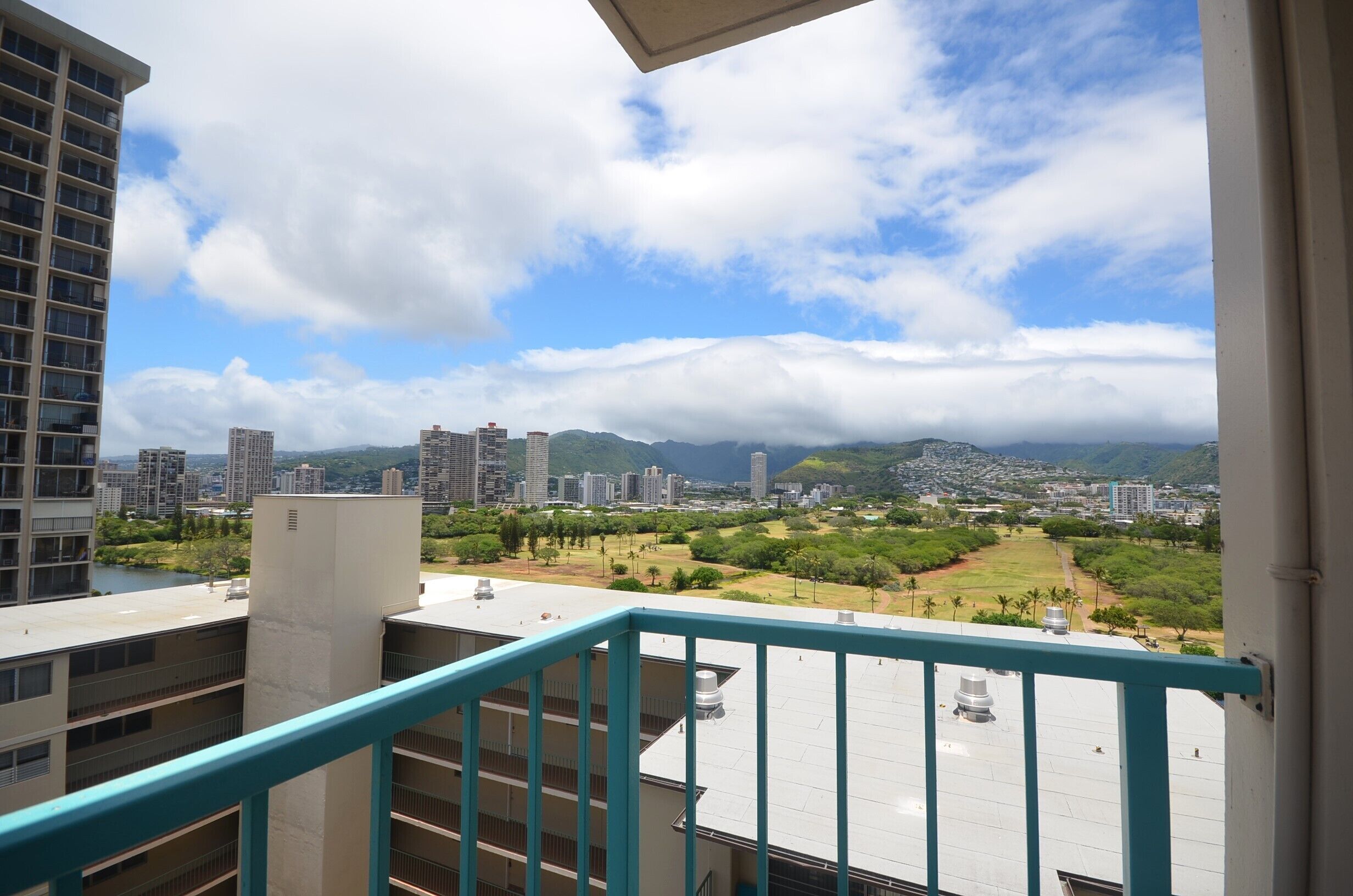 A balcony with a view of a cityscape, including high-rise buildings and a park with greenery.