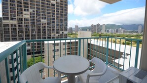 Een balkon met een tafel en stoelen, met uitzicht op een stadsgezicht met hoogbouw en groen.