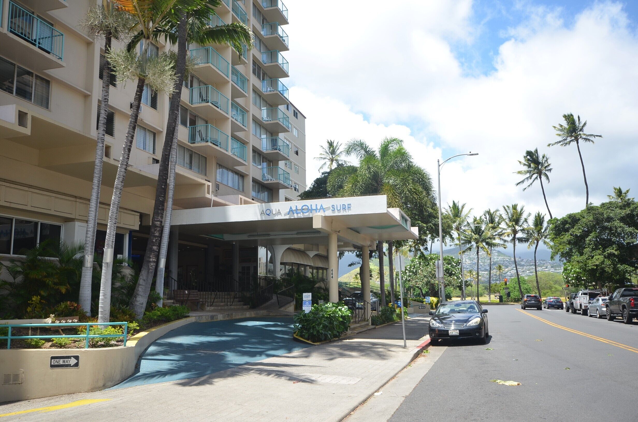 A hotel with a covered entrance, palm trees, and a view of the street.