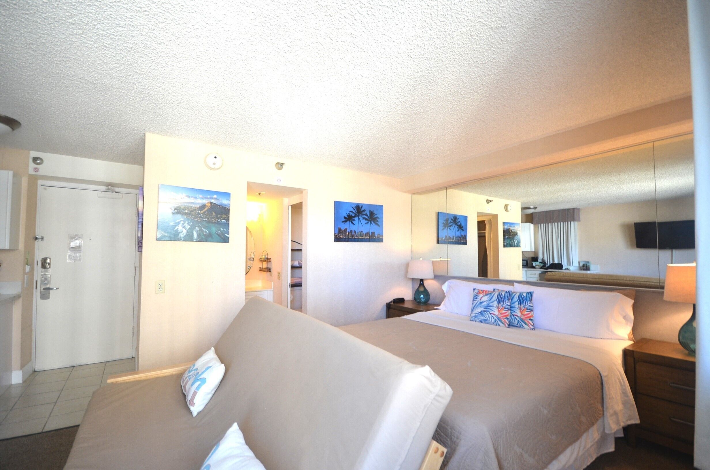 Una habitación de hotel con cama, mesitas de noche, una lámpara, televisor y decoración en la pared.