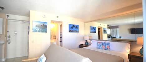 Una habitación de hotel con cama, mesitas de noche, una lámpara, televisor y decoración en la pared.