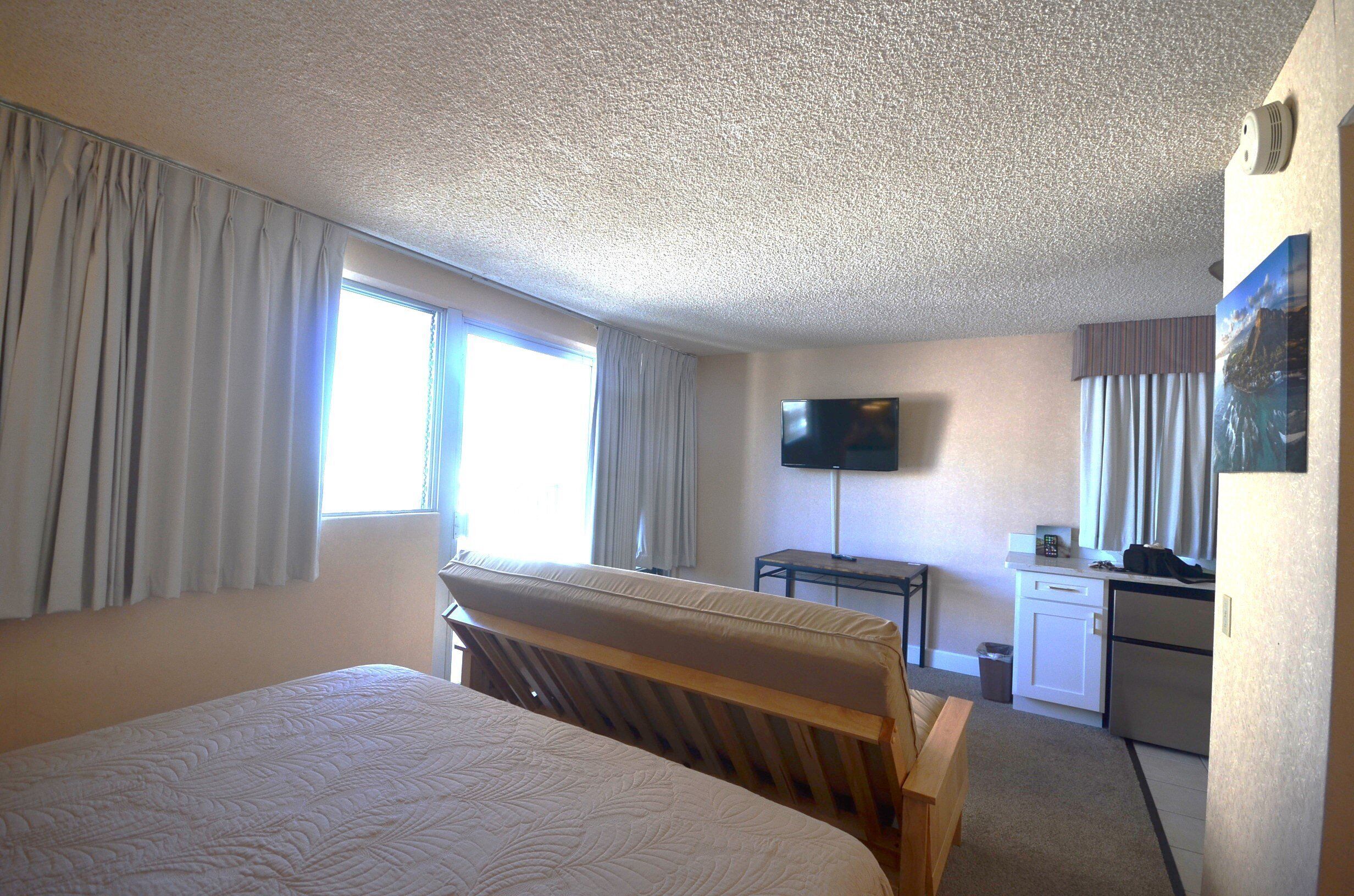 Habitación de hotel con dos camas, un escritorio, televisor y una kitchenette.