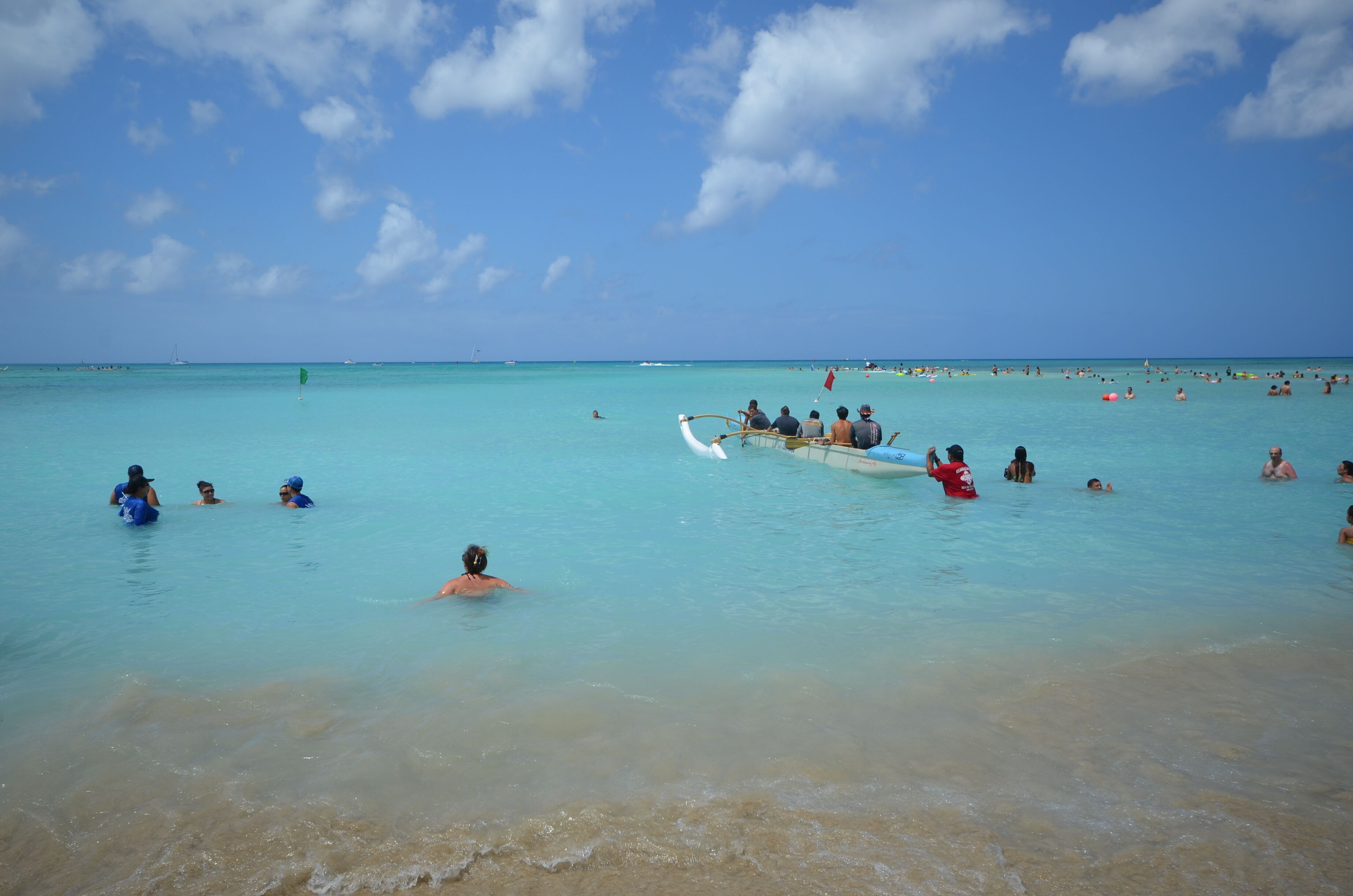 A beach with clear turquoise water, people swimming and a traditional boat with passengers.