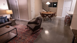 Een moderne woonkamer met een bruine leren fauteuil, een eettafel met stoelen, een kleurrijk vloerkleed en een trap op de achtergrond.