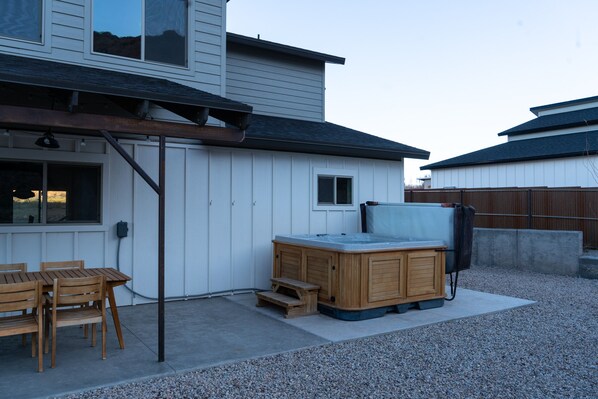 A backyard with a hot tub, wooden deck, and a covered patio area.