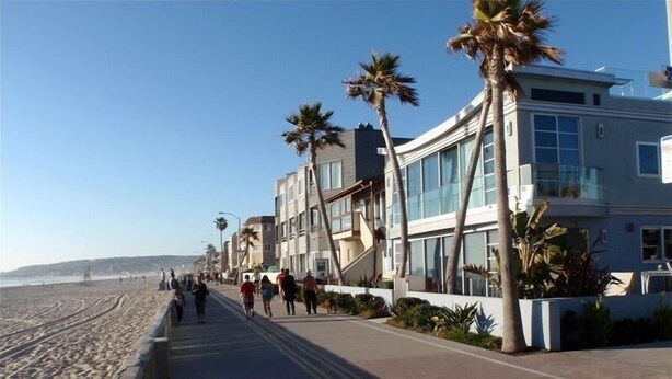 Eine Küstenpromenade mit modernen Gebäuden, Palmen und einem Strand im Hintergrund.
