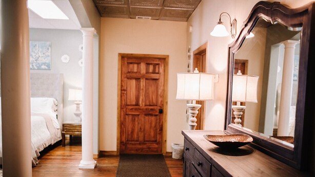 A hotel room with a wooden door, a vanity with a mirror, a bed, and a small rug on the floor. - Crossroads Flat:  Steps away from Rt. 66 & Carthage square (Carthage)