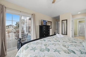 A bedroom with a large bed, a dresser, a sliding glass door to a balcony, and a framed picture on the wall. - Koinania Cottage | 245 ft from the Beach | Private Pool (Virginia Beach)