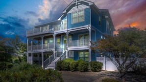 Une maison à deux étages avec un balcon au premier étage et une véranda avec des marches menant à l’entrée.