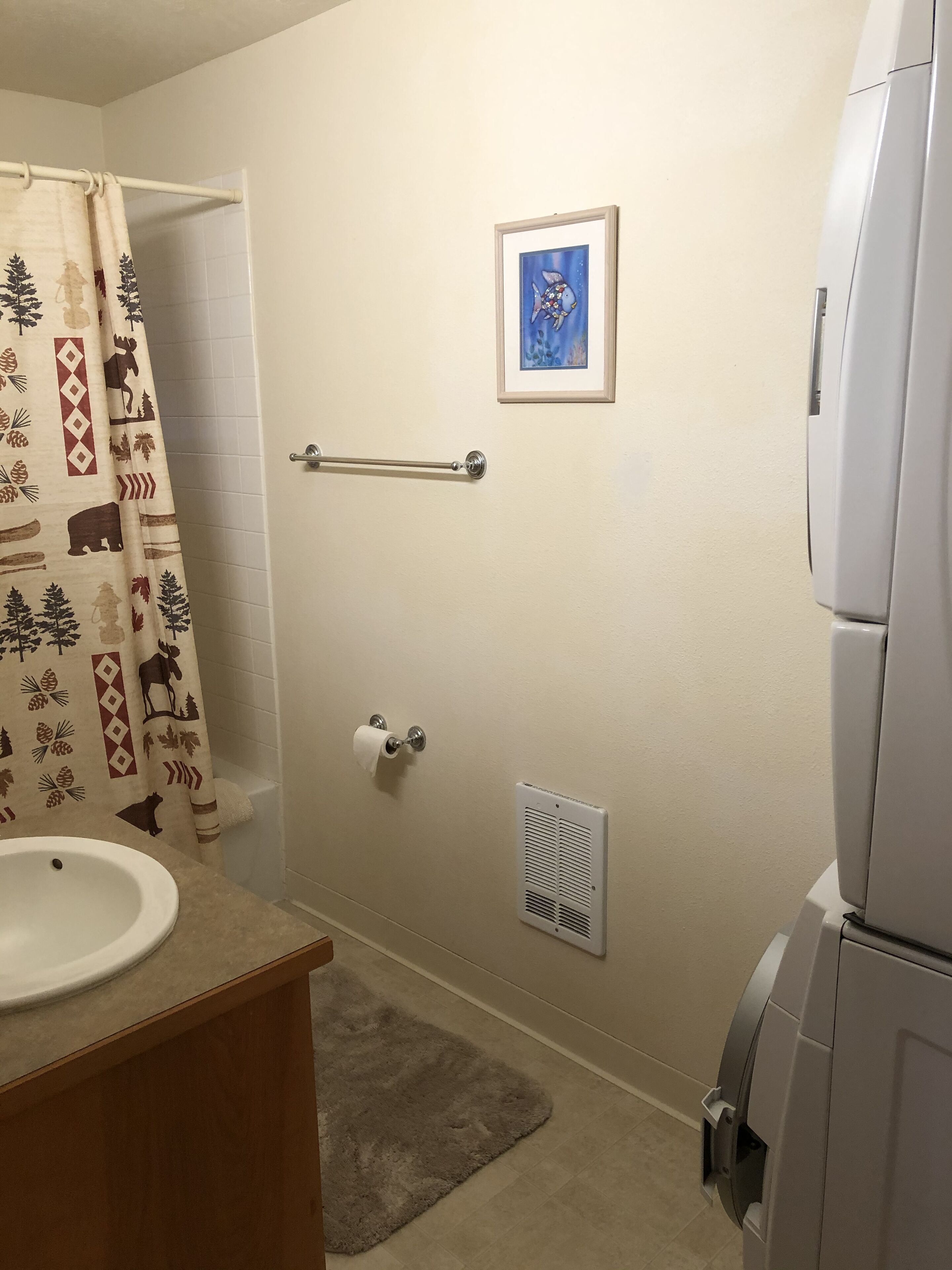 A bathroom with a toilet, sink, shower curtain, towel rack, framed picture, and a vent.