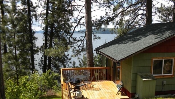 Una cabaña con terraza, una parrilla y vistas a un lago.
