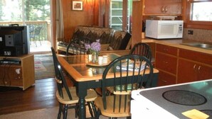 Un interior de cabaña acogedor, con comedor, sofá, televisión y cocina equipada con microondas.