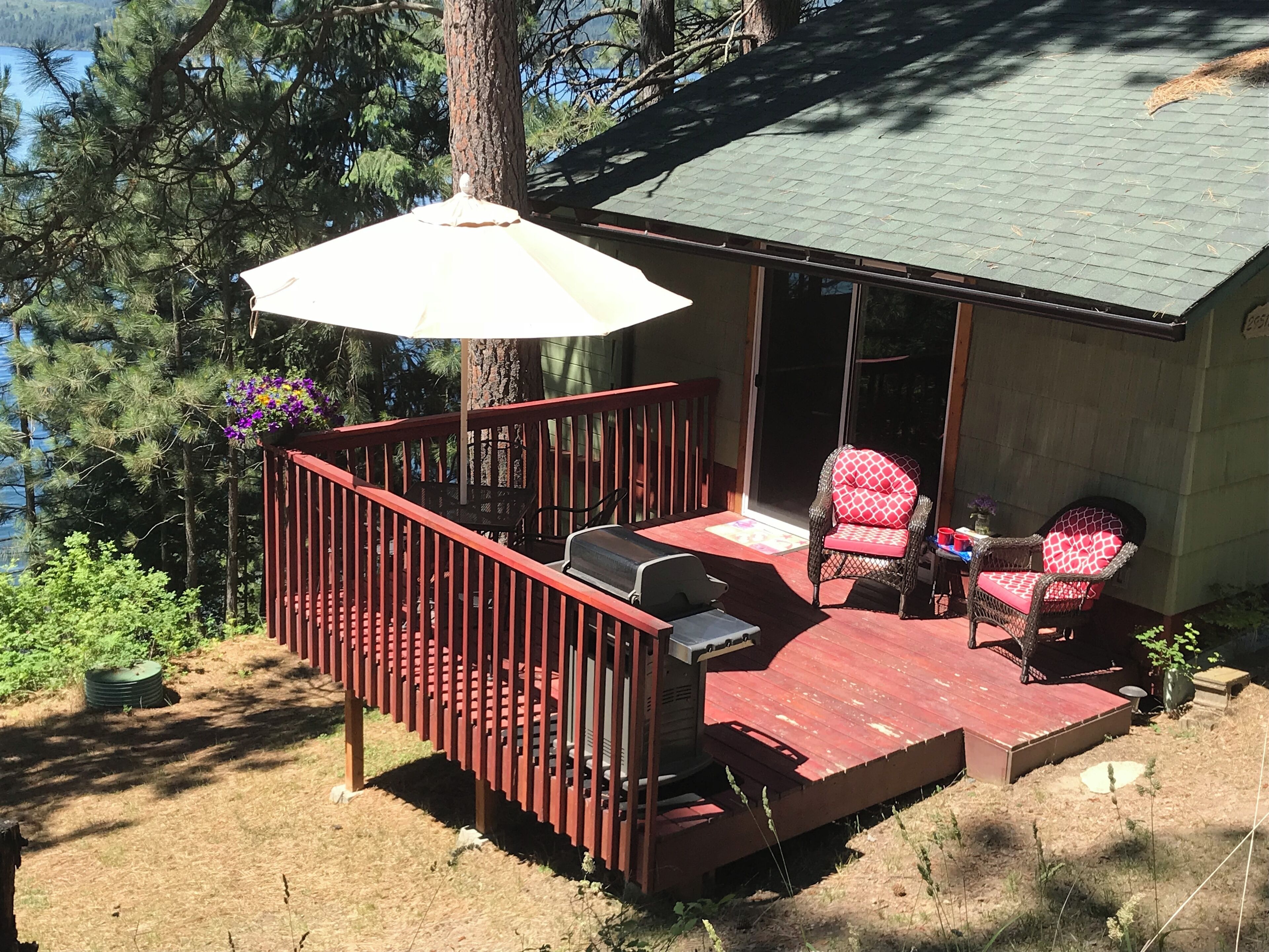 A deck with a grill, two wicker chairs, and a patio umbrella.