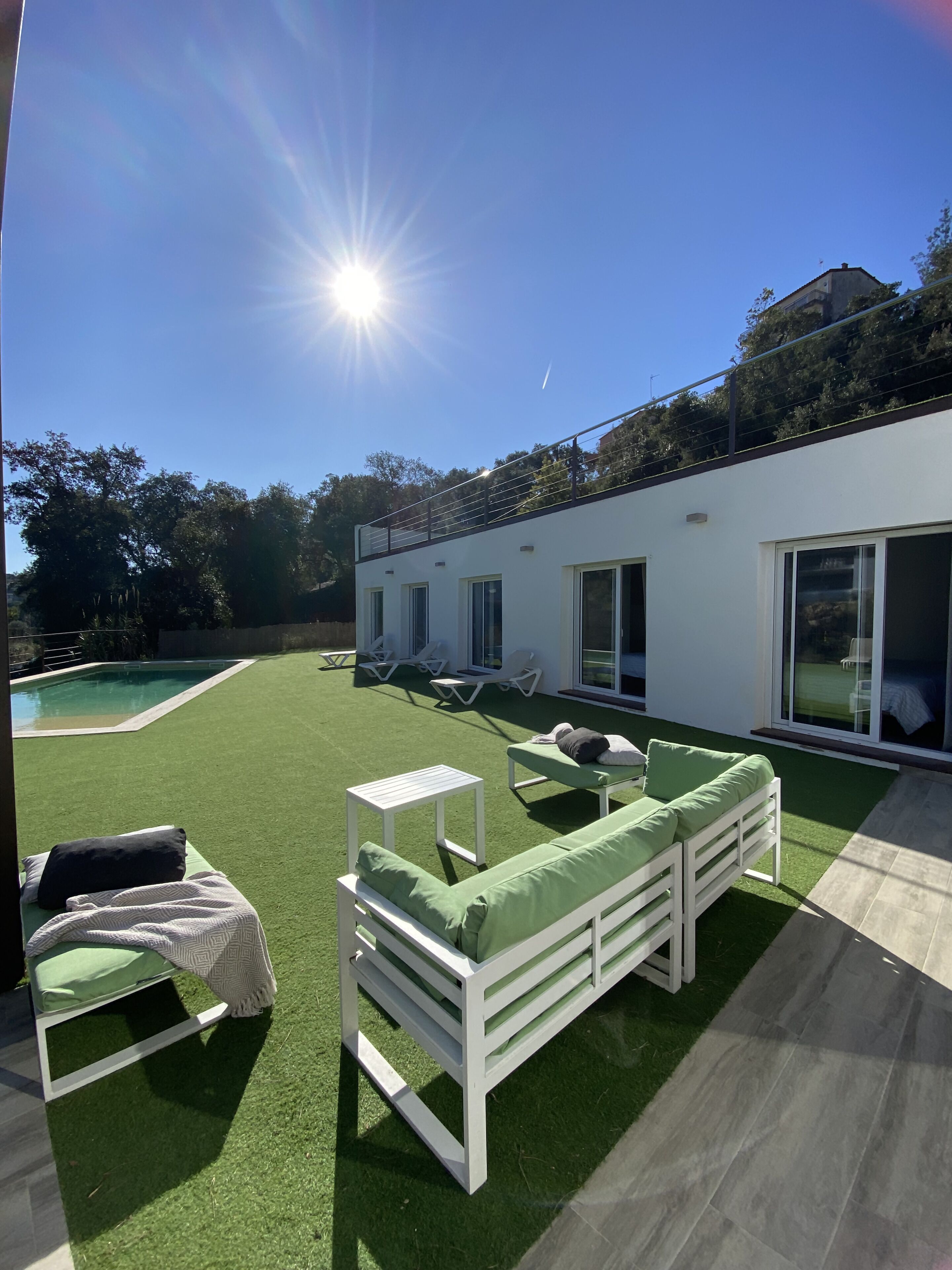 A modern outdoor living area with a pool, sun loungers, and a white building with large windows.