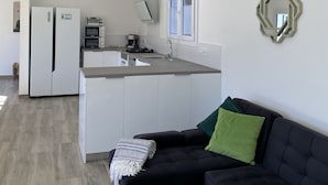 A modern kitchen with white cabinetry, a built-in oven, and a microwave. There is a black sofa with a green pillow and a patterned throw blanket. - Casa Rio de Oro with pool featuring beach area and barbecue. Calonge Costa Brava (Calonge)