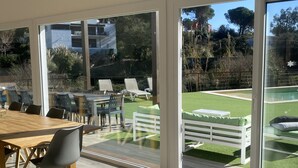 A modern interior with a wooden dining table and chairs, large sliding glass doors leading to a garden with a pool and outdoor seating. - Casa Rio de Oro with pool featuring beach area and barbecue. Calonge Costa Brava (Calonge)