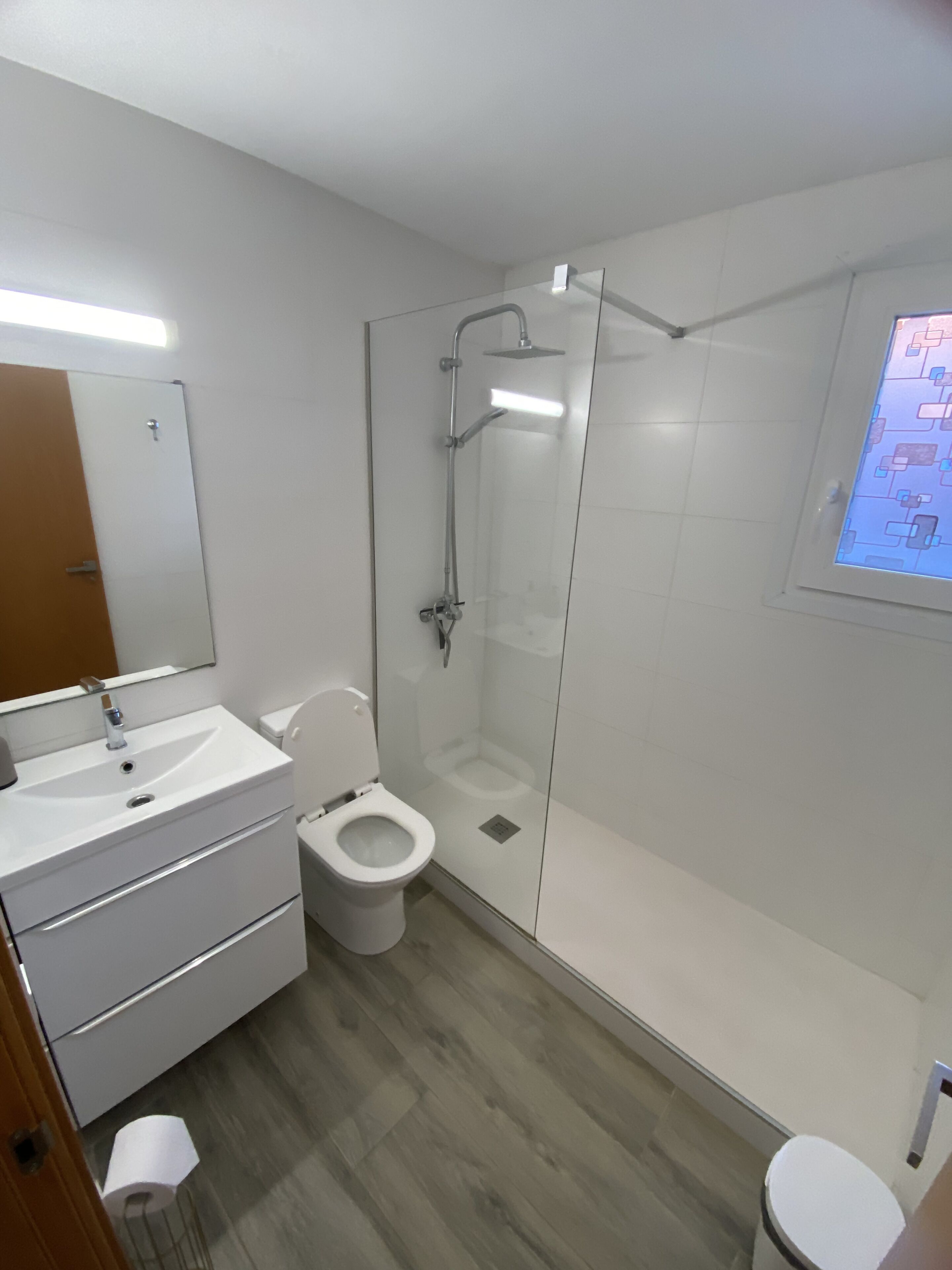 Moderni kylpyhuone, jossa on lasiseinällä varustettu suihku, valkoinen pesuallas ja wc.
