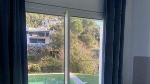 A bedroom with a bed, a nightstand, and a view of a swimming pool and greenery outside. - Casa Rio de Oro with pool featuring beach area and barbecue. Calonge Costa Brava (Calonge)