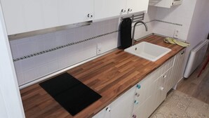 A kitchen with white cabinets, a wooden countertop, a black induction cooktop, a white sink, and a red radiator. - Deltamar 80 Solo Familias! (Xeraco Playa)