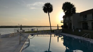 A swimming pool with a view of the sunset over water, surrounded by lounge chairs and palm trees. - Beach & Boating & Fishing Paradise! With 2 Kayaks Included!!! (St. Augustine)