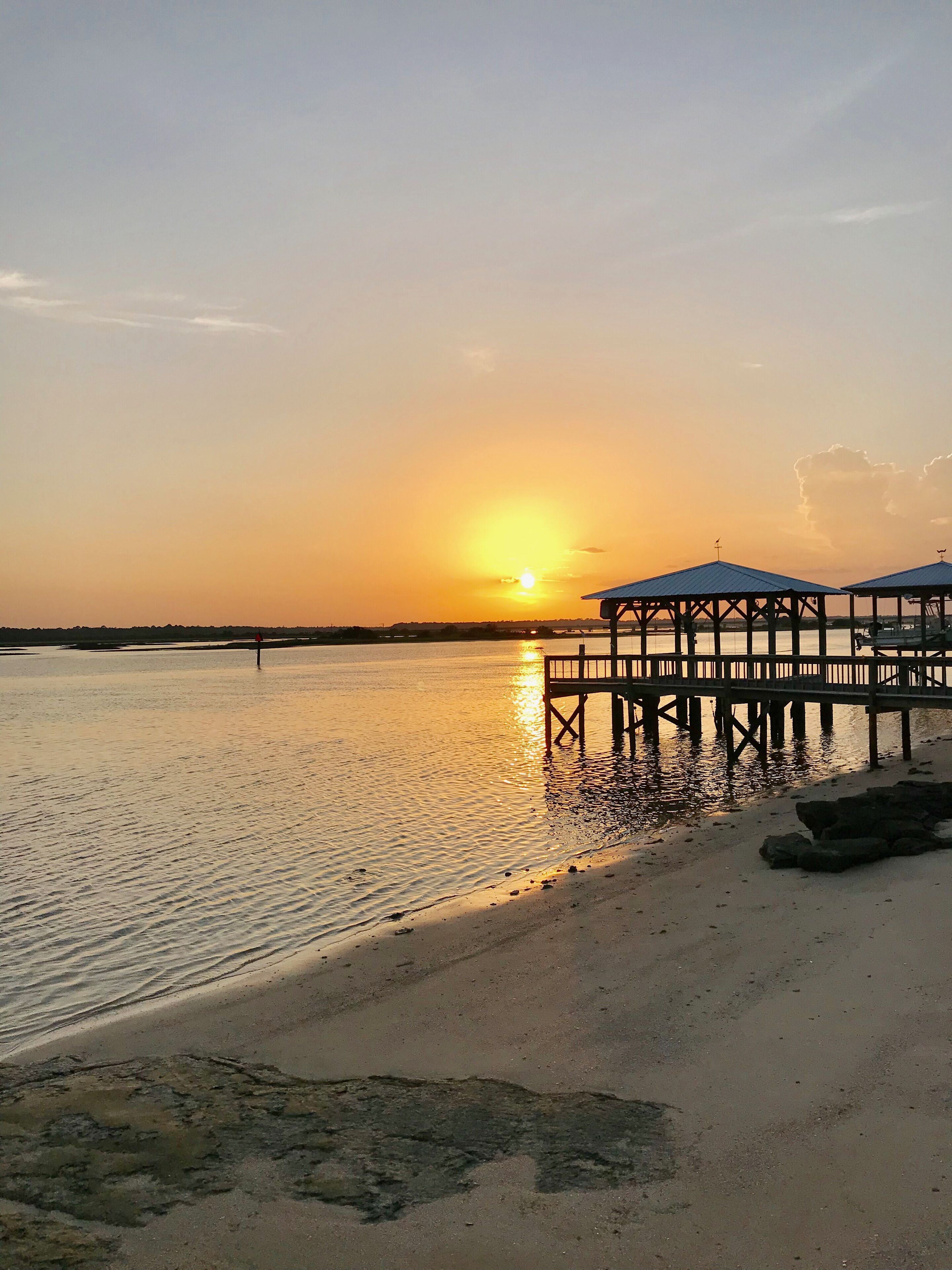 A sunset over a calm body of water with a pier extending into the water.