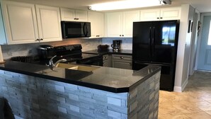 A kitchen with white cabinets, a black refrigerator, a microwave, a stove, and a sink. - Beach & Boating & Fishing Paradise! With 2 Kayaks Included!!! (St. Augustine)