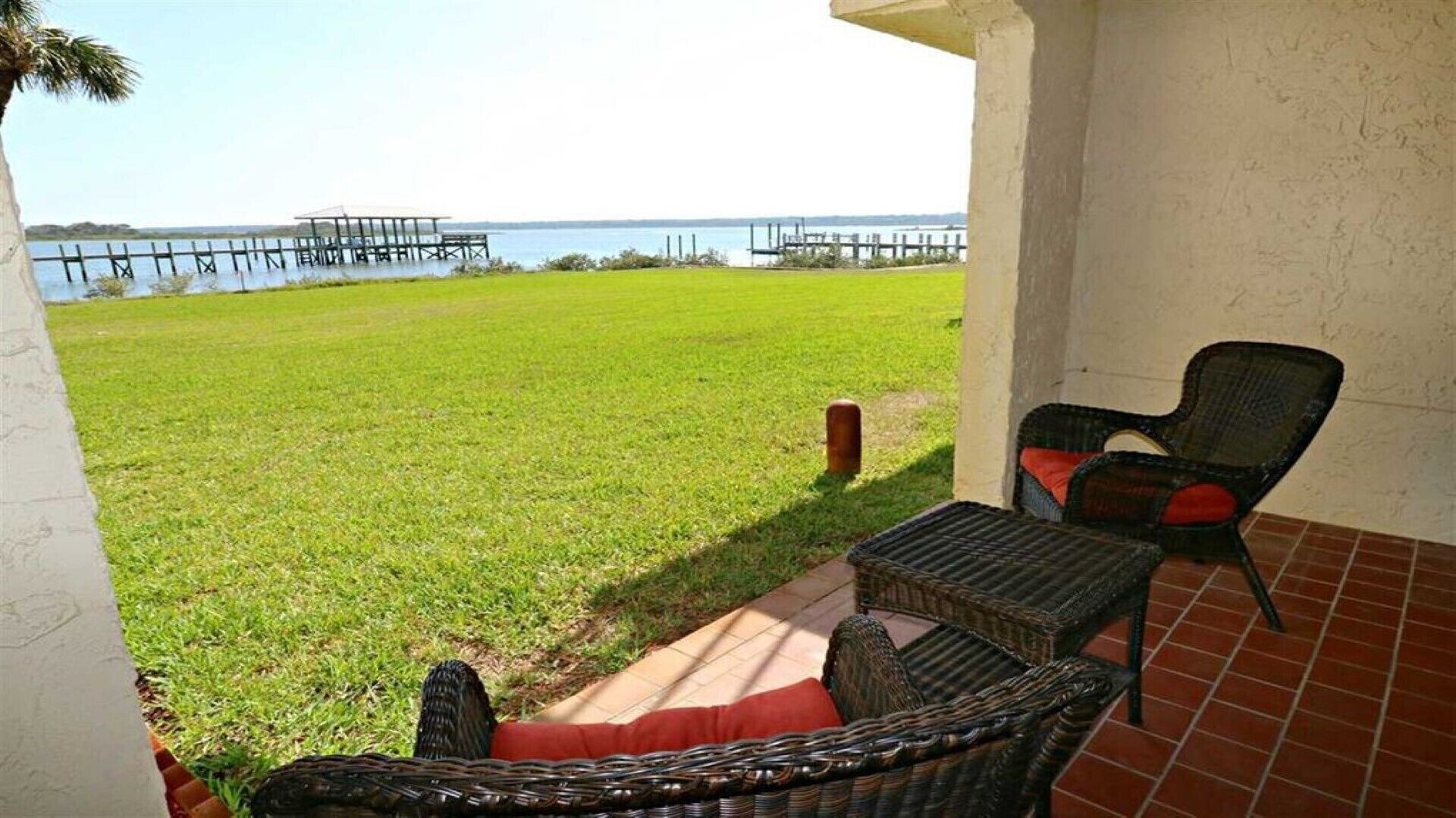 A patio with wicker furniture, a grassy lawn, and a view of a body of water with docks.