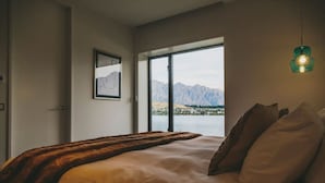 A bedroom with a large bed, a view of mountains through a window, and a hanging light fixture. - Lakehouse Joela | Award winning luxury home | Close to central Queenstown (Queenstown)