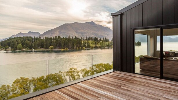 A modern building with a wooden deck overlooking a lake and mountains. - Lakehouse Joela | Award winning luxury home | Close to central Queenstown (Queenstown)