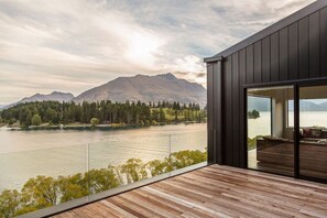 A modern building with a wooden deck overlooking a lake and mountains.