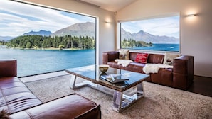 A modern living room with a large window offering a scenic view of a lake and mountains. - Lakehouse Joela | Award winning luxury home | Close to central Queenstown (Queenstown)