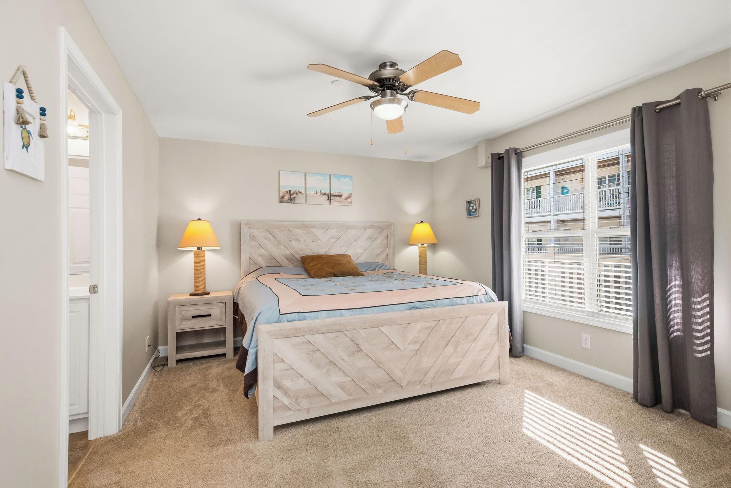 A bedroom with a bed, two bedside lamps, a ceiling fan, a window with blinds, and a door.