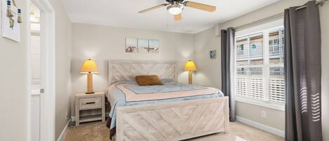 A bedroom with a bed, two bedside lamps, a ceiling fan, a window with blinds, and a door.
