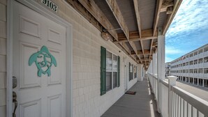 Um corredor com portas brancas, persianas verdes e teto de madeira.