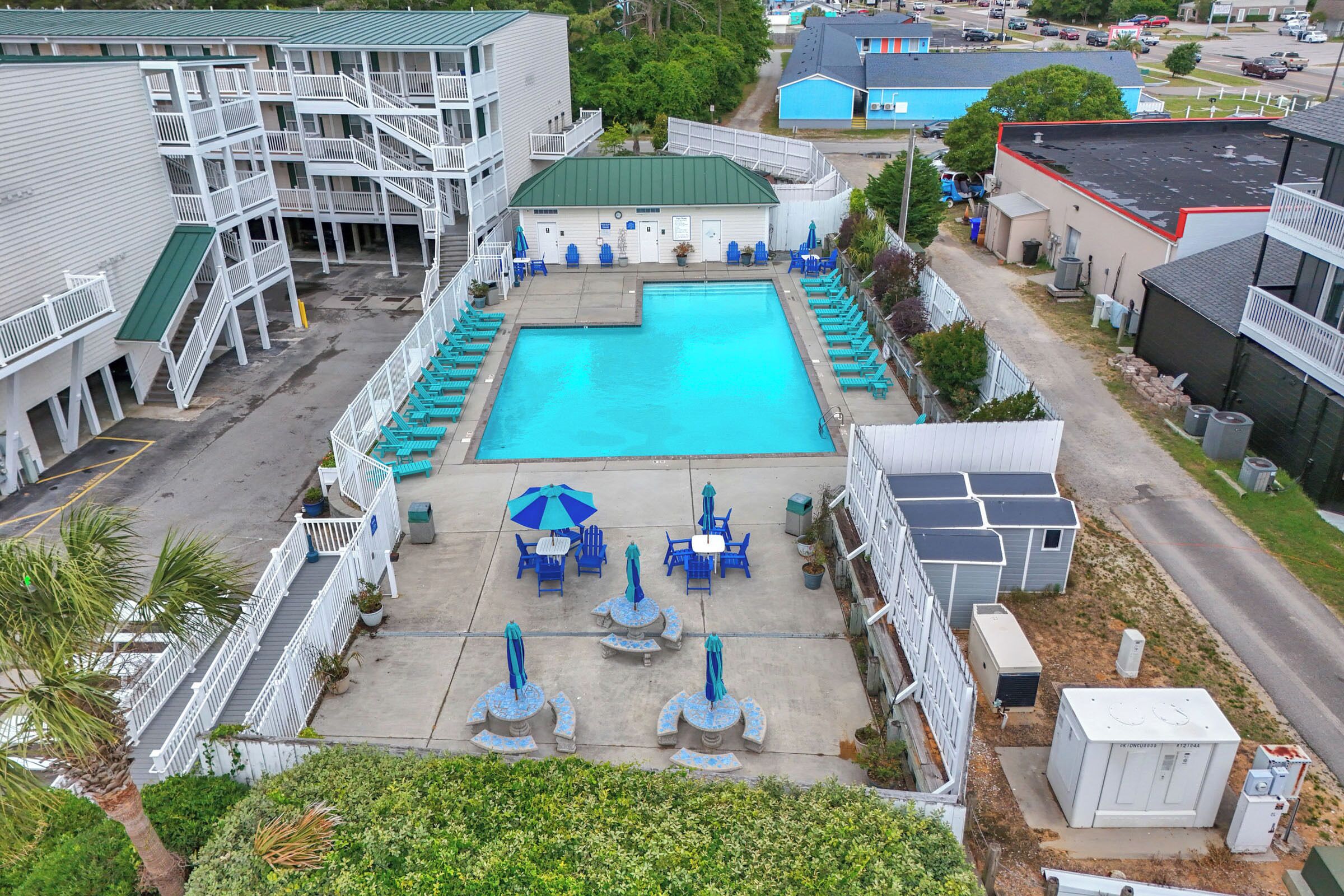 Una piscina con sillas de descanso y sombrillas, rodeada de edificios con balcones y una escalera.