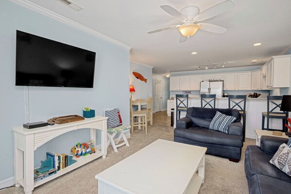 A living room with a flat-screen TV, a white coffee table, a dark-colored sofa, and a ceiling fan.