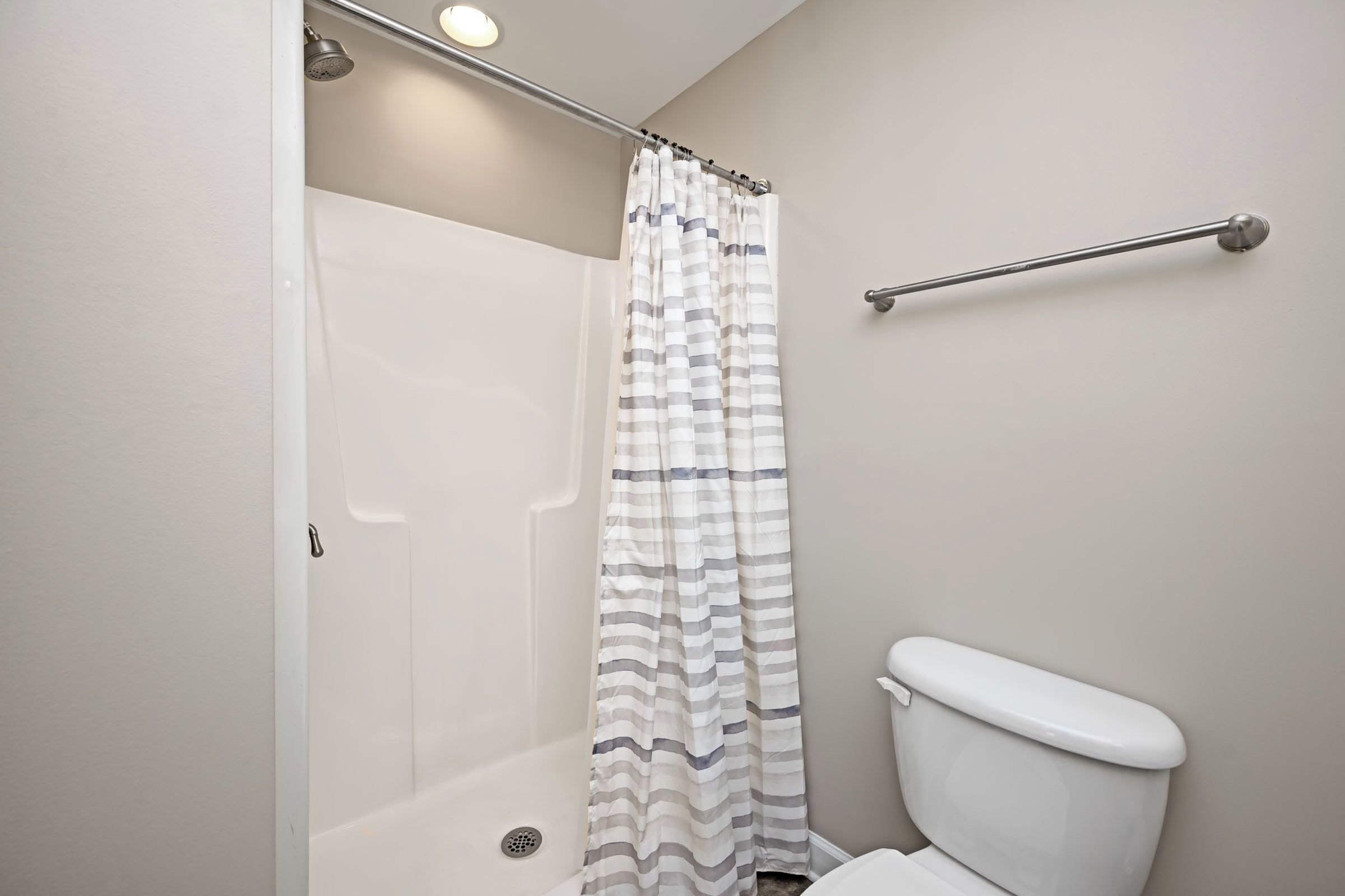 Un baño con ducha, inodoro y barra de apoyo.
