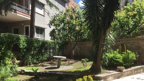 Un patio con un banco de piedra, rodeado de abundante vegetación y una palmera.