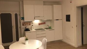 A compact kitchen with white cabinets, a coffee machine, and a sink. There is a dining table with chairs and a small potted plant.