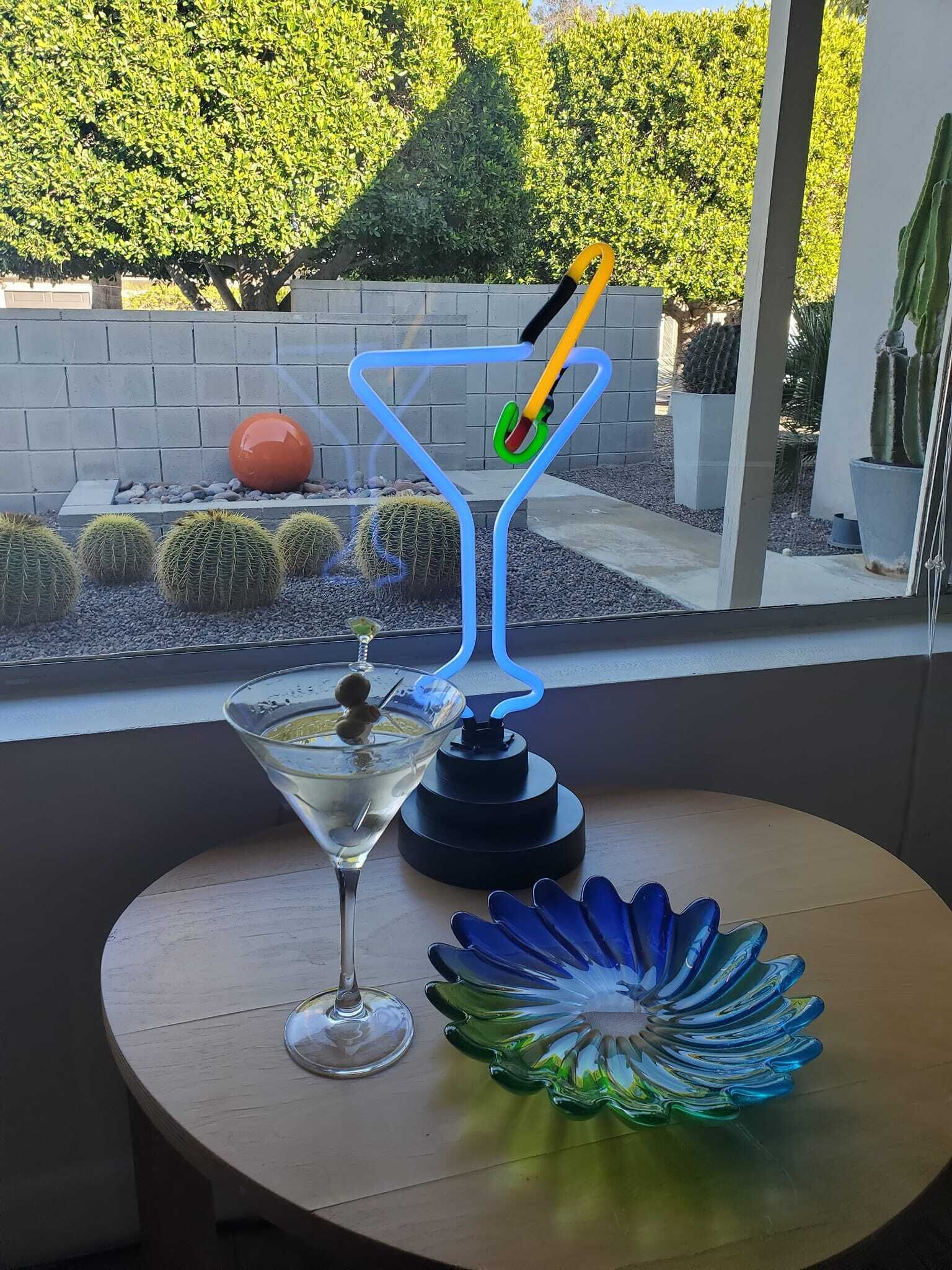 Ett bord med ett martiniglas, en blå och grön glasskål och en blå och grön glasskulptur.
