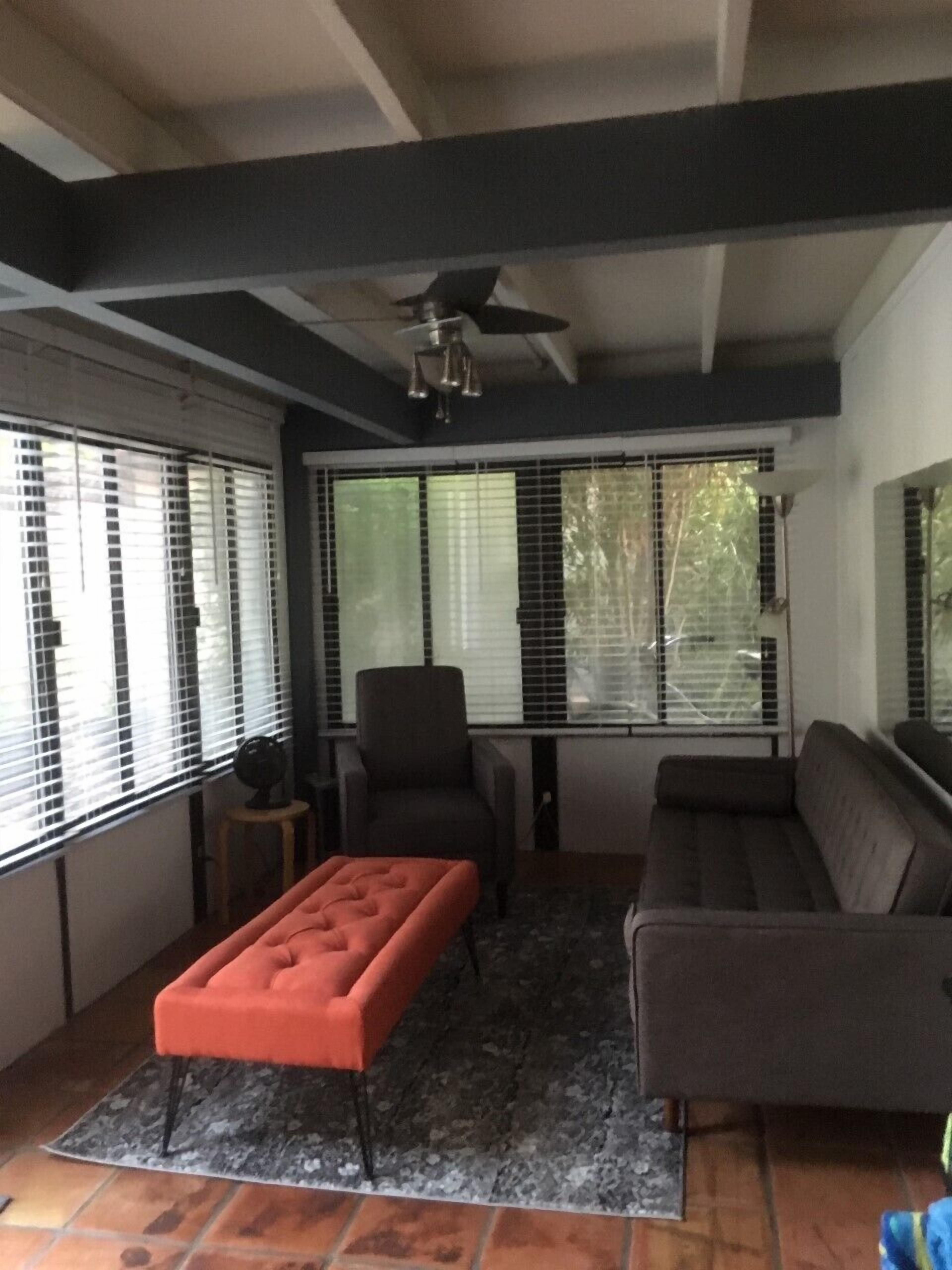 Un salon avec un ventilateur de plafond, un canapé, un pouf et un fauteuil.