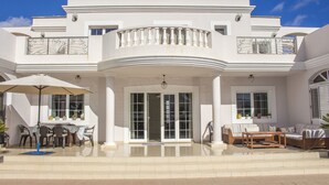 Une grande maison moderne dotée d’un vaste patio aménagé avec du mobilier d’extérieur et un grand parasol.