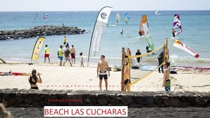 Un match de volleyball de plage avec un filet et des joueurs, une côte rocheuse et un ciel dégagé.