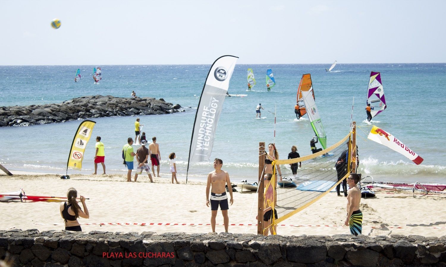 Un match de volleyball de plage avec un filet et des joueurs, une côte rocheuse et un ciel dégagé.