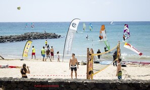 Un partido de voleibol de playa con red y jugadores, una costa rocosa y un cielo despejado.