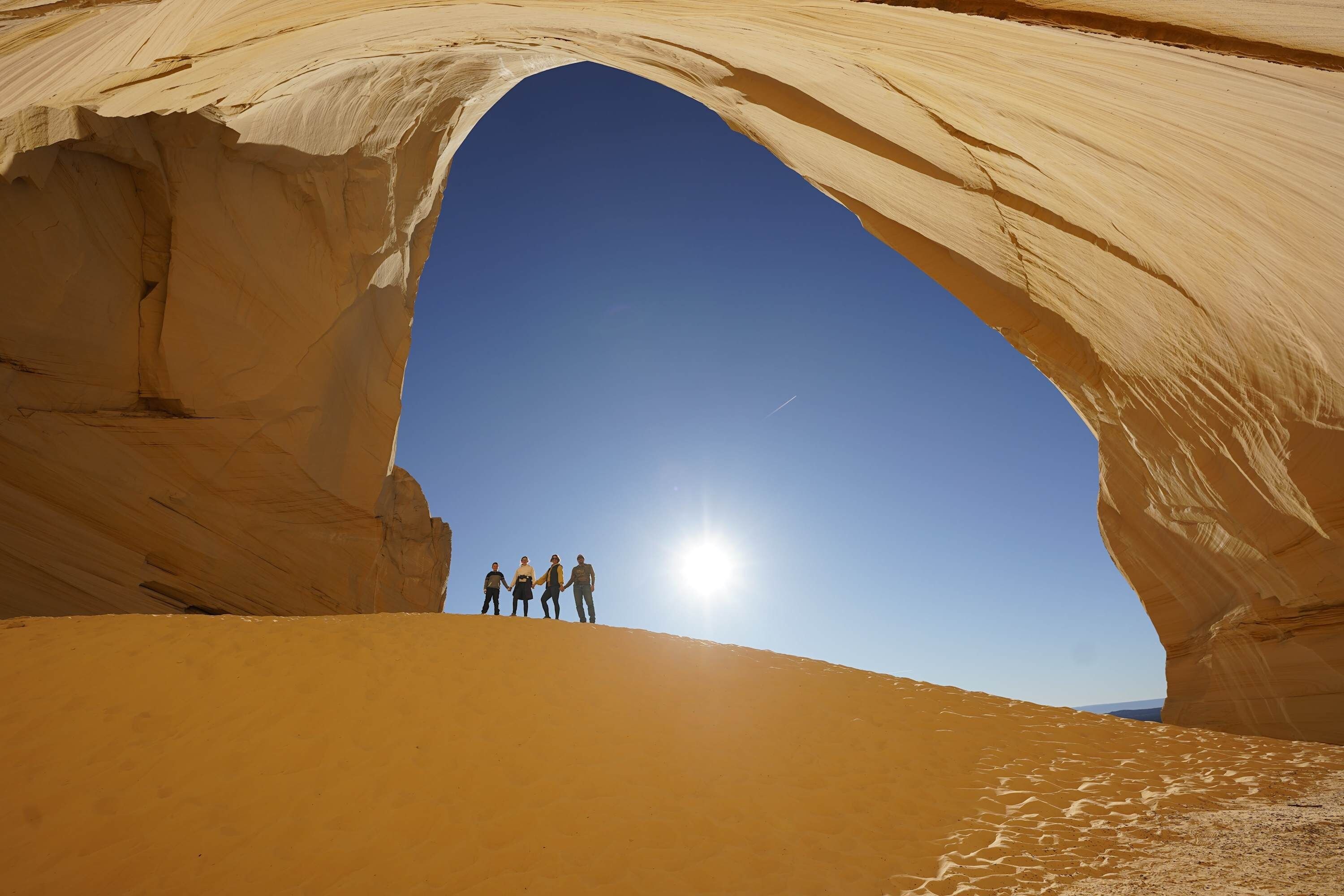 Une arche naturelle formée par des roches, avec un ciel dégagé et un groupe de personnes se tenant à sa base.